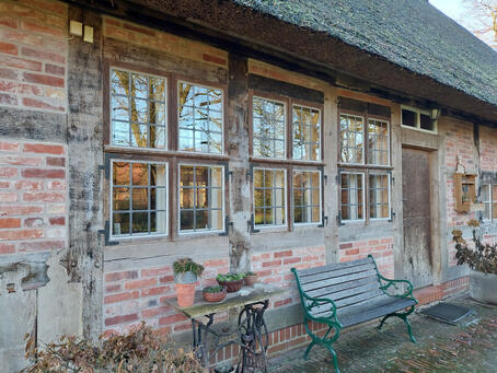 Uenzen, Hofstelle, Nordseite mit saniertem Fachwerk, Klöntür und an den Ständern angeschlagenen Fenstern und dem 2005 eingedecktem Reetdach (2023) Ursprünglich befanden sich lediglich das mittlere und das rechte Fenster sowie eine Tür in der Lucht. © Interessengemeinschaft Bauernhaus, Jenny Heinrichsdorff-Struß und Herbert Struß